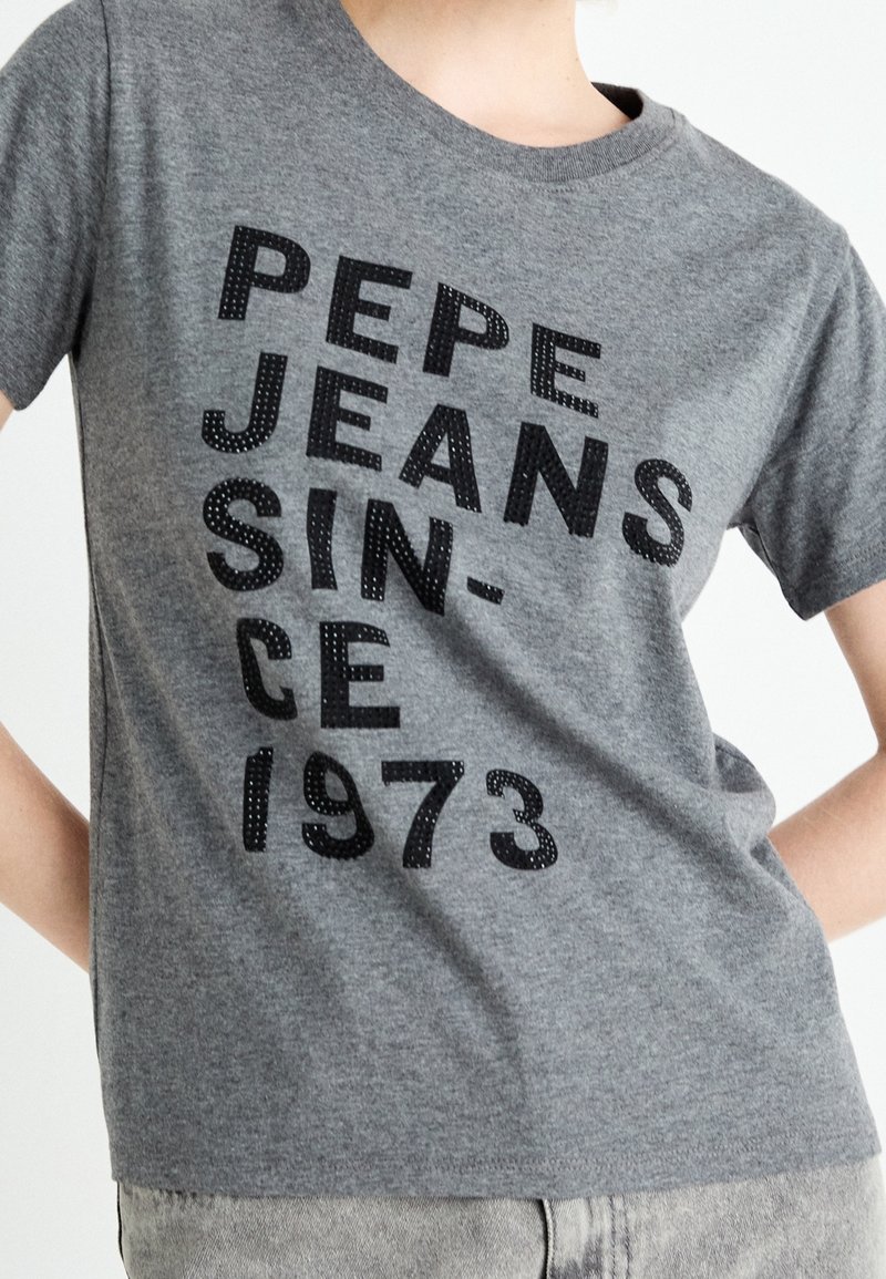 Camiseta de algodón gris con mangas cortas que presenta texto negro en relieve: "PEPE JEANS SINCE 1973", con un ajuste sencillo y clásico.