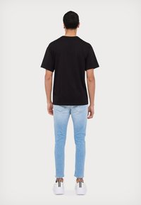 Schwarzes Baumwoll-T-Shirt mit kurzen Ärmeln, getragen mit hellblauen Slim-Fit-Jeans und weißen Sneakern mit schwarzen Streifen an der Ferse.