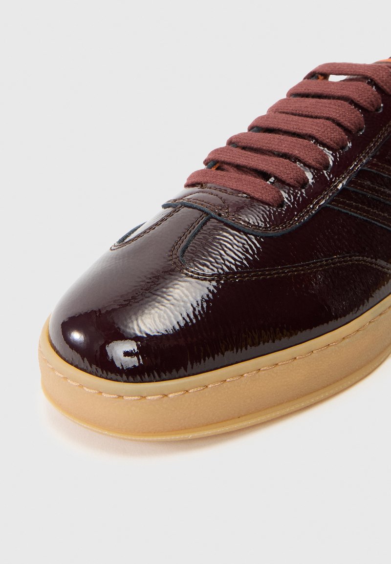 Burgunderfarvet patentlæder sneakers med brune snørebånd, rund tå og gummisål med cremefarvet kant og subtile rille detaljer.