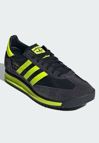 Černé a neonově žluté sportovní tenisky s svrchním materiálem z semiše a síťoviny, design se třemi pruhy, značkový jazyk, polstrovaná podrážka a texturovaná gumová podrážka.