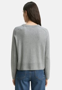 Grauer Pullover mit Rundhalsausschnitt, Rippbündchen und langen Ärmeln. Weiche Textur mit lockerer Passform, kombiniert mit blauen Jeans.