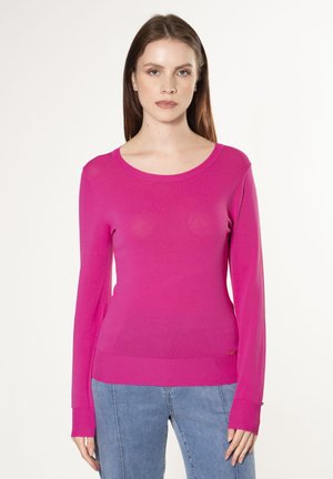 Fuchsia langer Pullover mit Rundhalsausschnitt, gerippten Bündchen und schlanker Passform. Weiche Textur. Kombiniert mit Denim-Hosen.