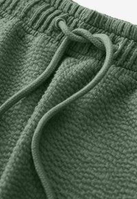 Tessuto verde con texture e chiusura con cordoncino. Presenta un motivo intrecciato e una vita elasticizzata per una vestibilità regolabile.