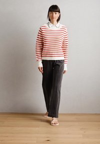 Red and white striped sweater with a ribbed texture, paired with dark gray wide-leg pants and light sandals; formal collar with scalloped edges.
