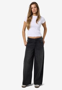 Zwarte wijde jeans met een hoge taille, gecombineerd met een aansluitend wit t-shirt. De jeans hebben voorzakken en een gestructureerde denimafwerking.