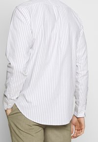 Svetle šedá a bílá pruhovaná košile s dlouhými rukávy, zapínacími manžetami a zakřiveným lemem, vyrobená z prodyšné látky.