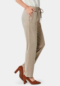 Beige tapse broeken met een elastische tailleband en trekkoord, zijzakken en een gladde textuur, gecombineerd met bruine hoge hakken.