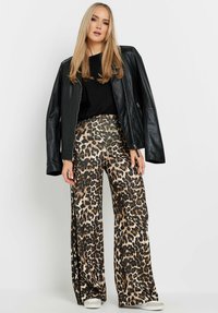 Veste en cuir noir, haut noir et pantalon large en imprimé léopard aux teintes tan, marron et noir. Texture lisse avec un design décontracté.