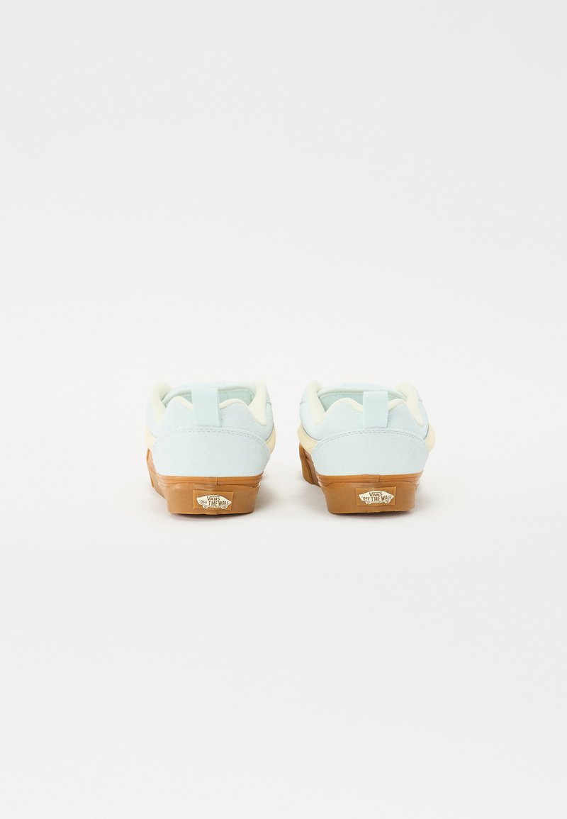 Baskets en daim bleu clair avec un col crème et une semelle en caoutchouc beige. L'étiquette sur le talon affiche le logo de la marque. Design simple et profil bas.