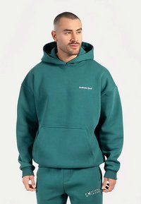 Groene katoenen hoodie met een voorzak en een klein wit logo op de borst. Relaxte pasvorm, geribbelde boorden en een verstelbare capuchon met trekkoord.