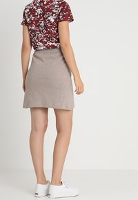 Brun stickad kjol med elastisk midja, kombinerad med en t-shirt i röd och vit kamouflageprint, bärs med vita sneakers. Har en enkel design.