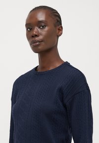 Sweatshirt en tricot marine avec un motif texturé, col rond et épaules tombantes. Fabriqué en tissu épais et confortable.