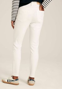 Valged kitsad teksad, millel on sile tekstuur ja kõrge vöökoht, kombineeritud juhuslike tossudega, millel on sinine ja kreemikas värvigamma. Triibuline pika varrukaga särk.