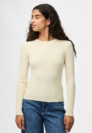 Haut à manches longues côtelé crème avec un col rond, design ajusté et texture douce, associé à un jean bleu taille haute.