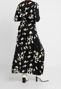 Larga vestido negro con un estampado abstracto en blanco y marrón, mangas largas y cintura ajustada. Combinado con botas blancas hasta el tobillo y un acabado texturizado.