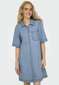 Denimkleid mit kurzen Ärmeln, vertikalen weißen Streifen, Knopfleiste und einer Brusttasche. Hellblaue Farbe und weicher Stoff.
