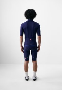 Námornícky cyklistický dres s krátkymi rukávmi a polstrovanými šortkami, vybavený zipsom, reflexnými akcentmi a logom značky na zadnej strane.