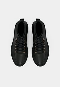 Fekete magas szárú csizmák sima bőrfelülettel, fém szemekkel és fekete fűzőkkel. Lekerekített orr és párnázott gallér kialakítás.