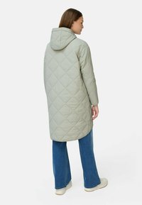 Lys grøn quiltet lang frakke med hætte, der har et diamantmønster. Kombineret med vide blå jeans og hvide sneakers.