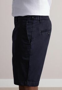 Marineblaue Baumwollshorts mit flachem Frontdesign, zwei vorderen Taschen und einer einzelnen Rückentasche, die mit einem Knopf gesichert ist. Glatte Textur.