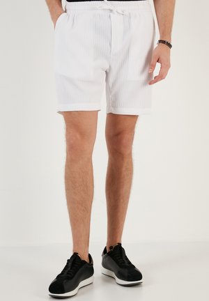 Hvide, ribbede shorts med elastisk talje og snøring. Med omkrøllede kanter og lommer. Sammen med sorte sneakers.