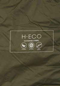 Tkanina w oliwkowym kolorze o gładkiej fakturze z białą metką. Na metce podkreślono teksty "H-ECO", "tkanina ekologiczna" oraz ikony dotyczące zrównoważonego rozwoju, przyjazności dla środowiska i odporności na wodę.