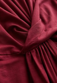 Tissu rouge foncé tordu et rassemblé, montrant une texture lisse et des plis avec un éclairage doux.