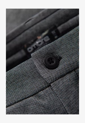 Tela de patrón en blanco y negro con un tejido texturizado, que presenta un botón de plástico negro y una etiqueta visible con la marca "Ombre".