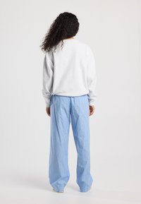 Lichtgrijze sweatshirt, losse pasvorm. Blauwe en witte gestreepte broek met brede pijpen en oranje accenten. Zachte textuur, minimalistisch ontwerp.