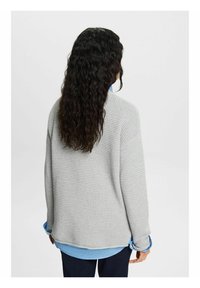 Grijze wafelstructuur trui gezien vanuit de rug, met een comfortabele pasvorm en lange mouwen over een blauwe blouse.