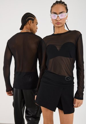 Schwarzes Mesh-Oberteil mit langen Ärmeln und einer schwarzen trägerlosen Innenschicht, kombiniert mit einem enganliegenden schwarzen Miniröckchen mit seitlichem Akzent.