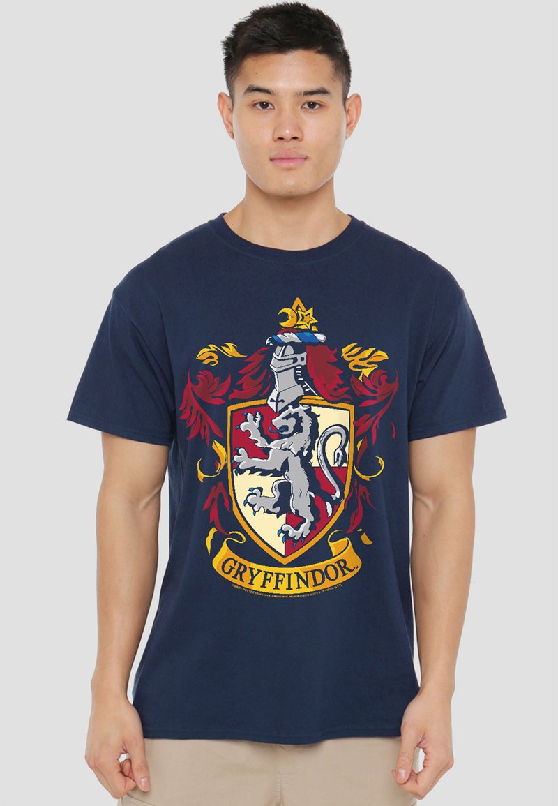 Young man wearing navy blue T-shirt with Gryffindor crest featuring a lion, helmet, and decorative red and yellow flourishes.
