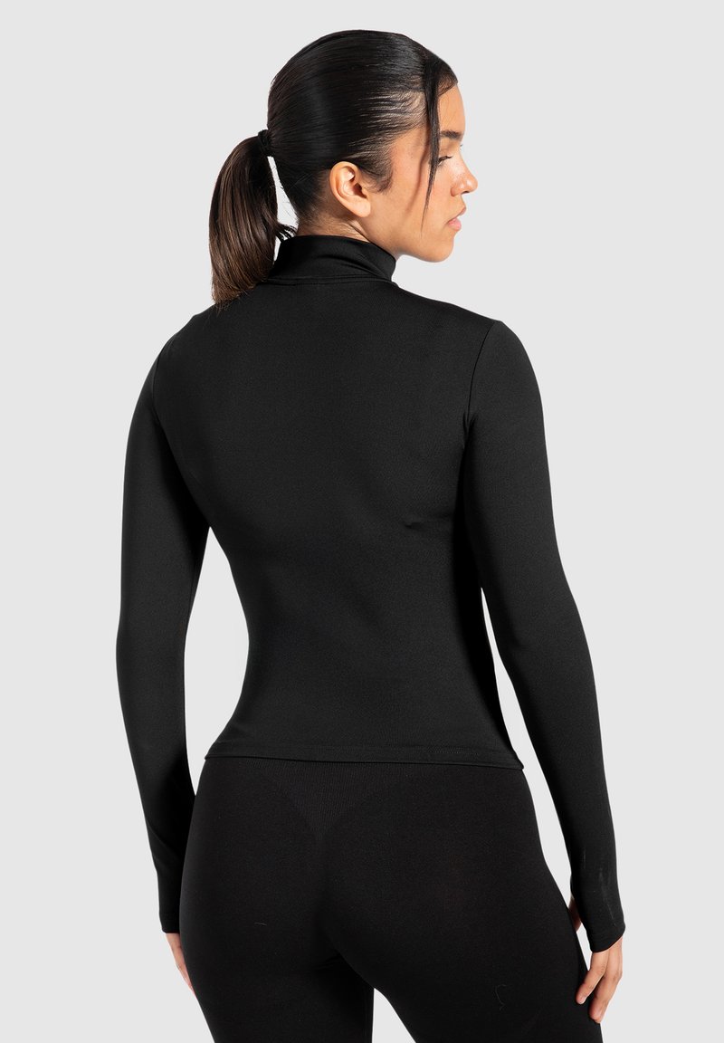 Schwarzes Langarmoberteil mit einem hohen Kragen, taillierter Passform, glatter Textur und ohne erkennbare Muster. Kombiniert mit schwarzen Leggings.