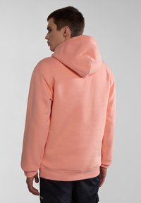 Sudadera de color durazno con capucha ajustable, puños y dobladillo acanalados. Textura suave y ajuste relajado, vista desde la parte de atrás.