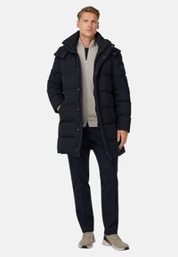 Svart puffermantel med hög krage, med framknappar och sidofickor, bärs över en ljusgrå topp och marinblå byxor.