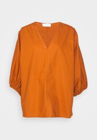 Blouse ample couleur rouille, avec un col en V et des manches 3/4 bouffantes resserrées par des poignets élastiques, confectionnée en tissu léger.