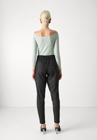 Mintgrön långärmad topp med off-shoulder-design, matchad med mörkgrå tapered byxor som har resårmidja och sidofickor.