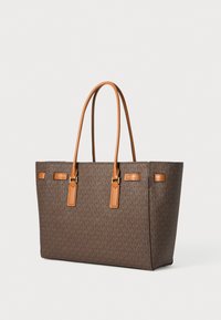 Bolso tote en lienzo marrón con monograma y detalles en cuero color marrón claro. Presenta herrajes dorados y una forma rectangular estructurada.