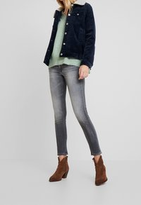 Marinblå kordflorsjacka med en lätt fleecekrage, mintgrön stickad tröja, urblekt grå smala jeans och bruna klackade ankelstövlar.