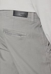 Pantalon gris clair avec poche passepoilée à l'arrière et étiquette en cuir noir de la marque Jack & Jones au-dessus de la poche, porté avec une chemise de couleur claire.