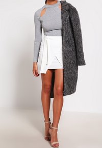 Haut gris à manches longues avec des détails découpés aux épaules, associé à une jupe portefeuille blanche. Accessoirisé d'un manteau gris texturé et de talons couleur nude.