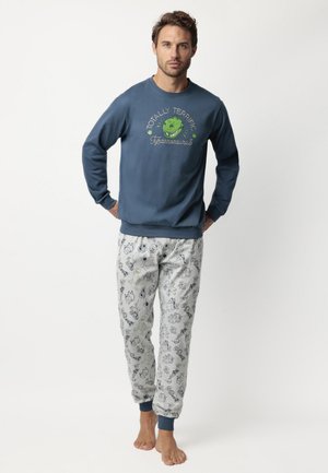 Sudadera azul con un gráfico de dinosaurio verde y diseño de texto, combinada con pantalones de pijama gris claro que presentan varios patrones caricaturescos.