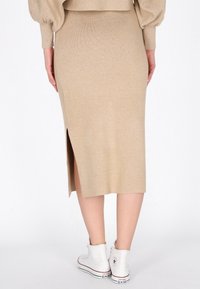 Beige midi hame, jossa on sivureikä, yhdistettynä valkoisiin korkean varren tennareihin. Hameessa on ribbikuviointi ja tiivis siluetti.