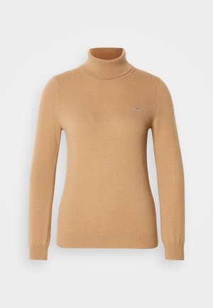 Beige turtleneck-genser laget av myk strikket stoff, med lange ermer og en subtil merkevarelogo på brystet. Ribbestrikkede mansjetter og kant.