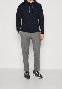 Sudadera azul marino con cordones ajustables, bolsillo frontal, pantalones grises ajustados y zapatillas multicolores con acentos blancos y logo.