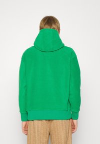 Felpa verde con un grande cappuccio regolabile, polsini e orlo a costine. Tessuto morbido e liscio, con un design semplice e senza loghi visibili.