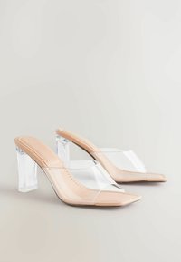 Mules nude à talons hauts avec un bout pointu, dessus en PVC transparent et talon bloc transparent. Fini lisse avec des détails de couture subtils.