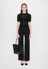 Top nero a coste a maniche corte, pantaloni neri a vita alta, ballerine nere a punta e una grande borsa a tracolla nera con dettagli bianchi. 