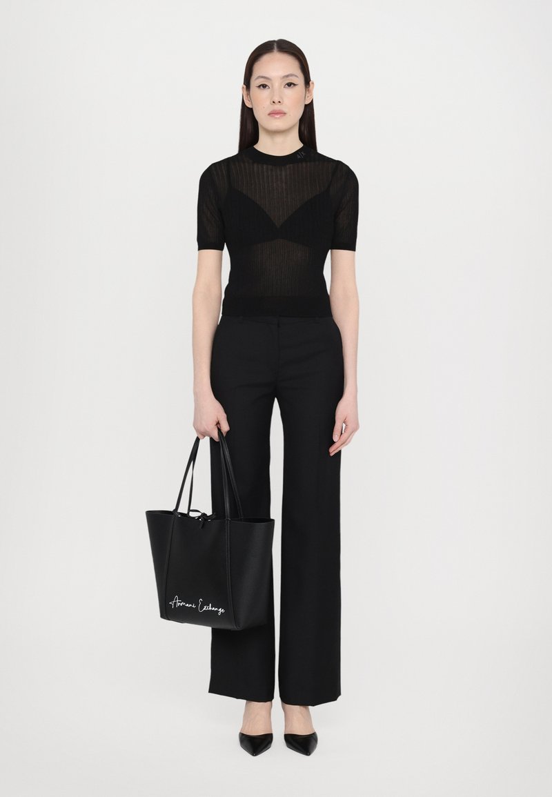 Top nero a coste a maniche corte, pantaloni neri a vita alta, ballerine nere a punta e una grande borsa a tracolla nera con dettagli bianchi.