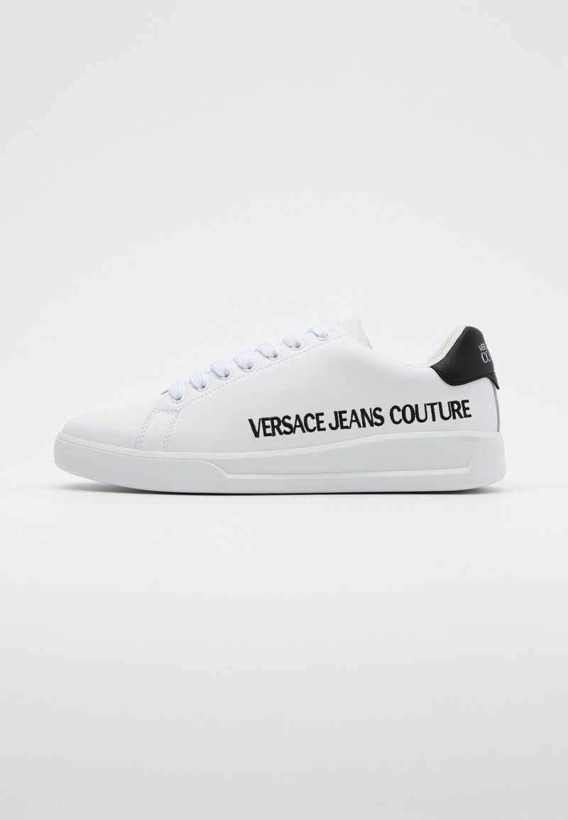 Baskets blanches avec détail noir au talon, lacets blancs et "Versace Jeans Couture" imprimé en lettres noires épaisses sur le côté.